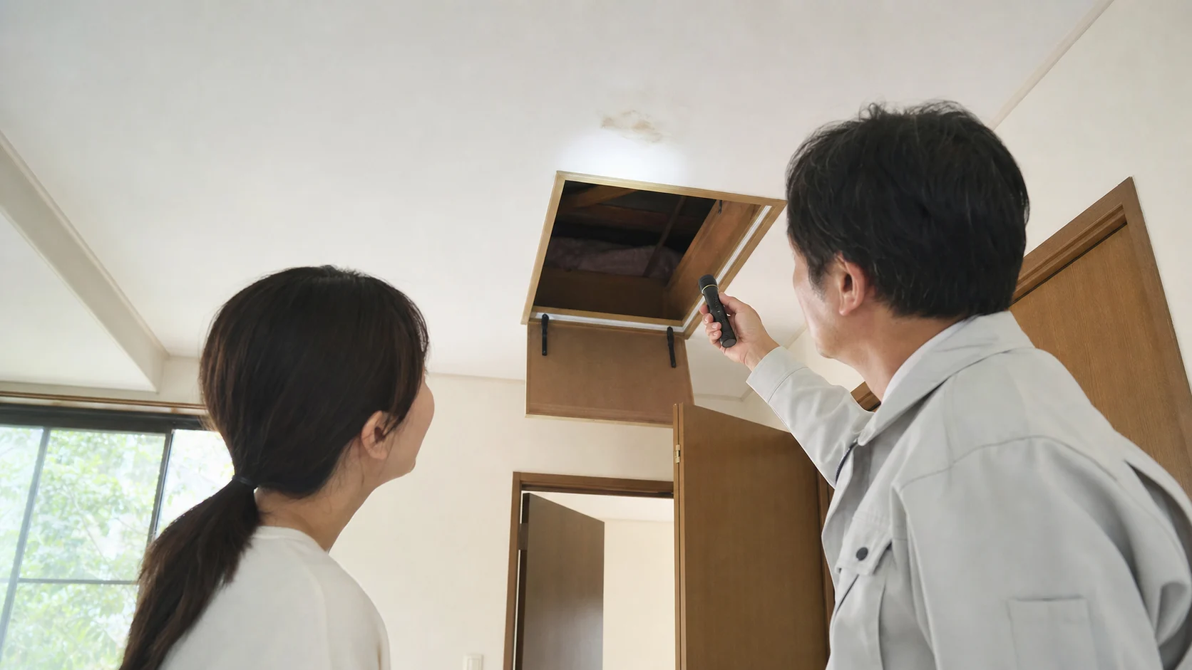 天井裏の点検口から雨漏りの痕跡を確認する日本の住宅点検の挿絵